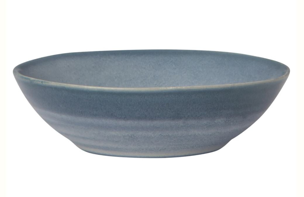 The Danica 5.5" Aquarius Bowl is a shallow, round ceramic piece featuring a smooth, matte finish in varying shades of blue. It has slightly sloping sides and showcases a subtle gradient from darker blue at the base to lighter blue near the rim.