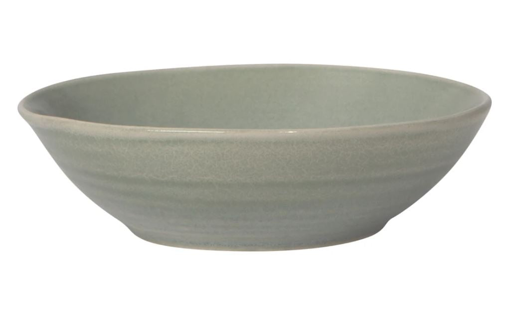 The Danica 5.5" Aquarius Bowl is a light gray, round ceramic dish featuring a smooth, slightly flared rim and a shallow depth. It has a subtle, horizontally brushed texture that lends it a simple yet elegant appearance. The bowl is empty and set against a white background.